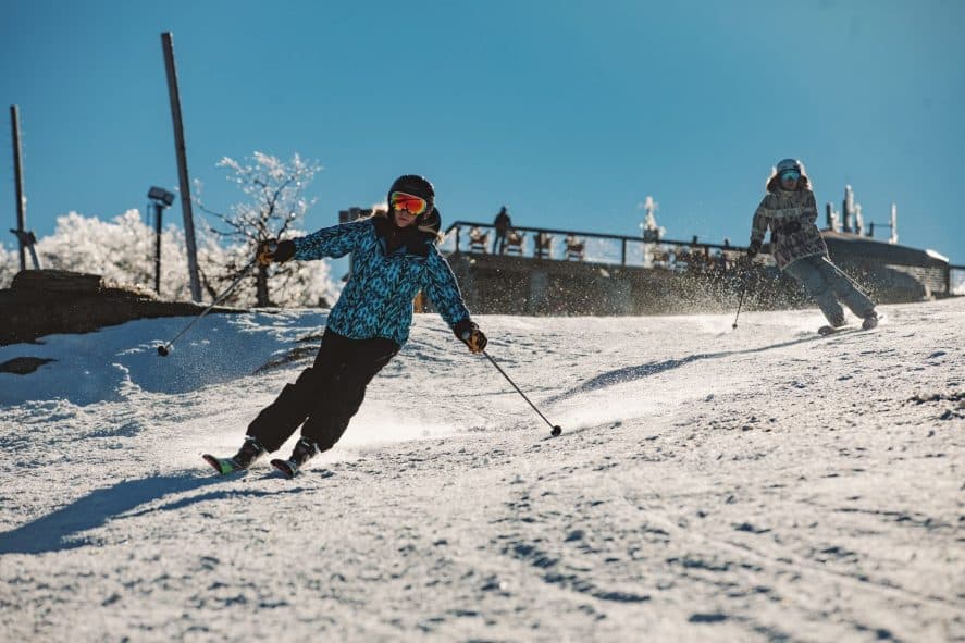 Two Skiiers on Beech Mountain Slope with Beech Mountain Brewing Patio in Background